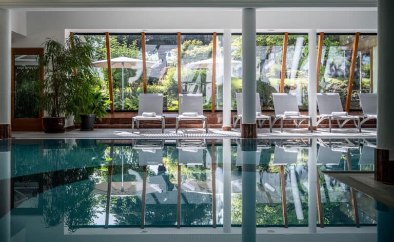 Hochwertiger Innenpool mit großen Fenstern, umliegende Liegen und entspannte Atmosphäre im Spa.