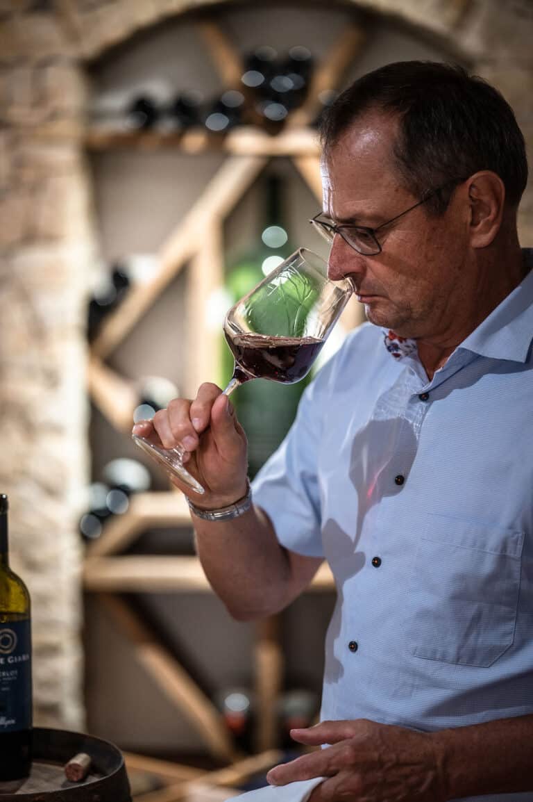 Altehrwürdiger Mann riecht konzentriert an einem Glas Rotwein bei Verkostung.