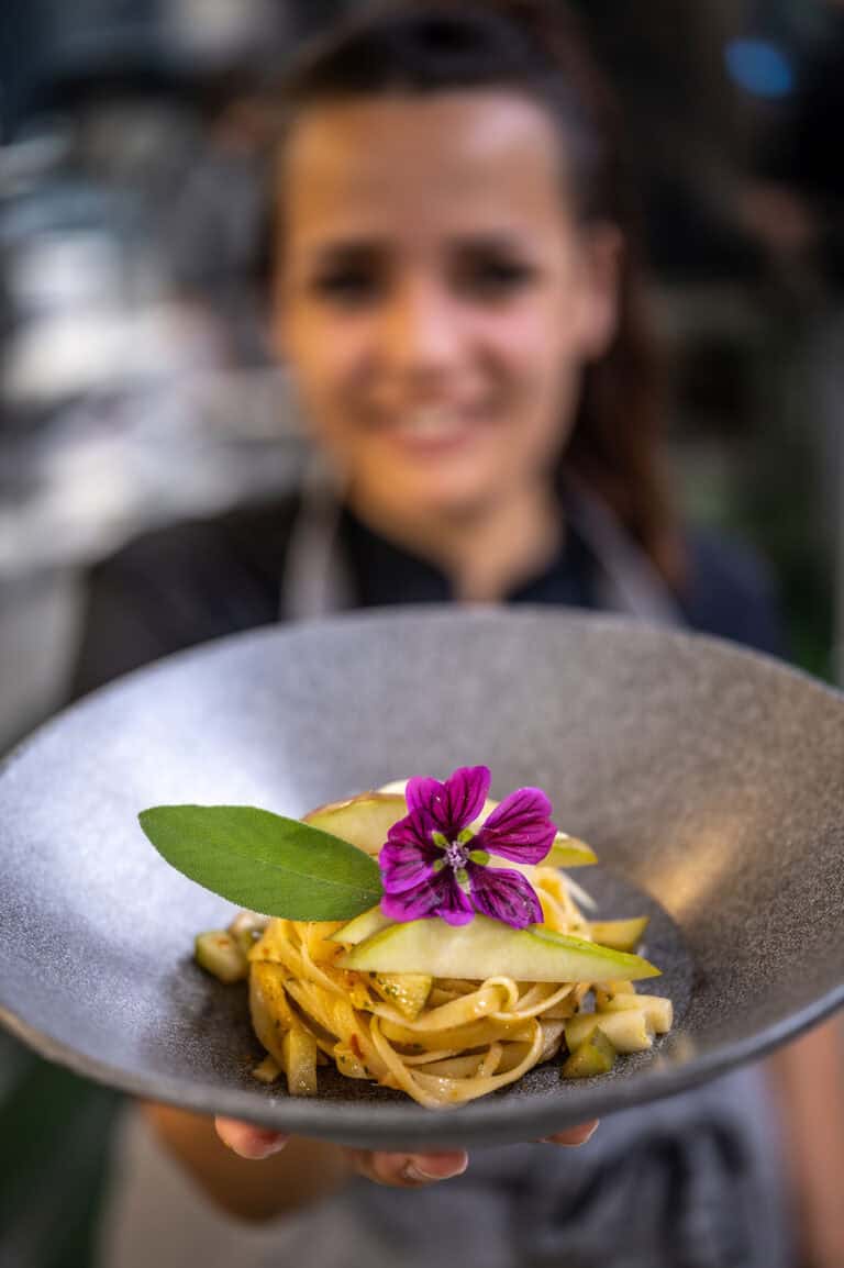 Hochwertige Pasta mit essbarer Blume, präsentiert von einem professionellen Koch unter angenehmer Atmosphäre.