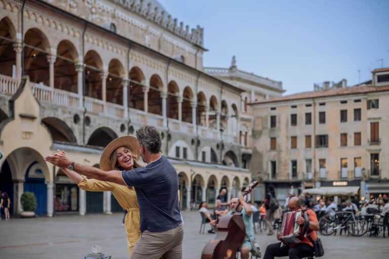 Hübsches Paar tanzt auf einem öffentlichen Platz, umgeben von Musikern und Passanten in einer historischen italienischen Stadt.