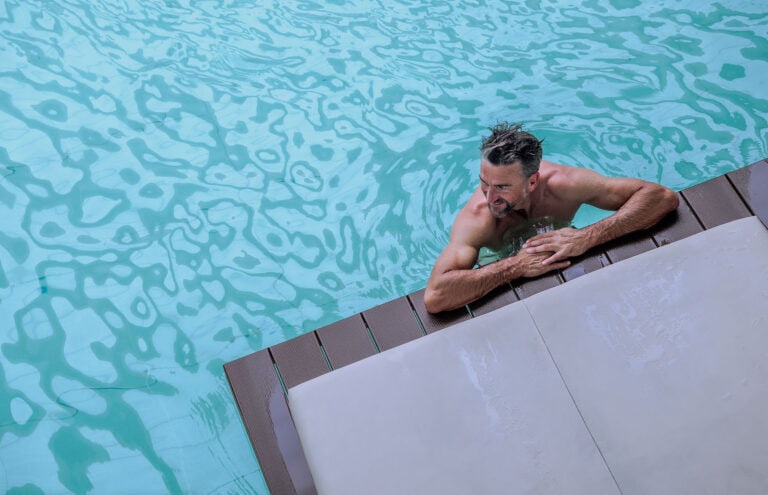 AltText: Mann entspannt im Schwimmpool, lächelnd, bei warmem Wetter im öffentlichen Schwimmbad.