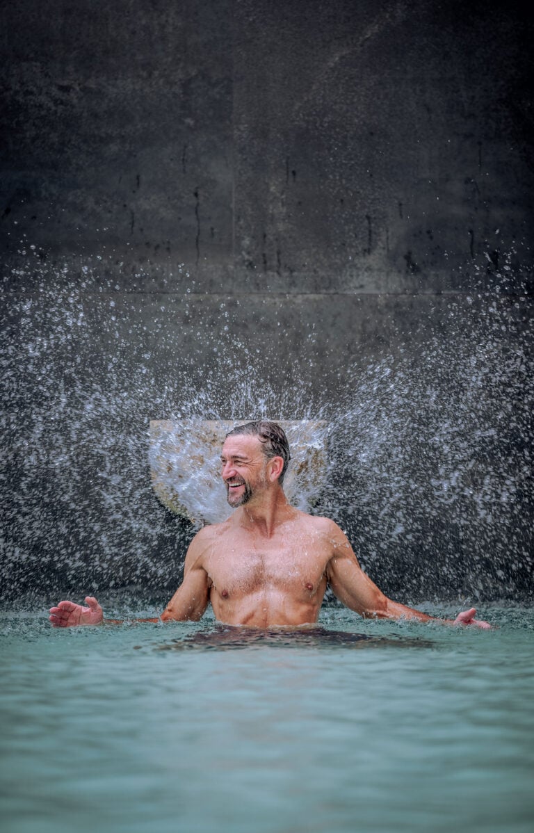 Mann entspannt im Wasser mit Wasserfall im Hintergrund, gelassen und glücklich.